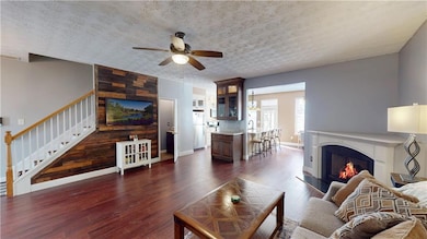 Living room with a ceiling fan, stairs, a textured ceiling, dark wood-style flooring, and a glass covered fireplace