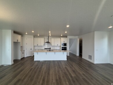 Kitchen featuring white cabinets, dark wood-style flooring, a center island with sink, decorative backsplash, and wall chimney range hood