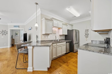 Kitchen with appliances with stainless steel finishes, a sink, a breakfast bar area, ornamental molding, and light wood-style floors