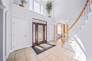 Entryway featuring ornate columns, ornamental molding, light tile patterned floors, a towering ceiling, and stairs