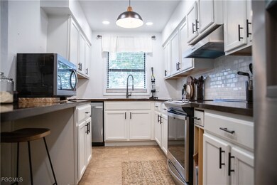 Kitchen with dark countertops, tasteful backsplash, appliances with stainless steel finishes, under cabinet range hood, and white cabinetry