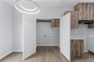 Washroom featuring hookup for a washing machine, cabinet space, light wood-type flooring, and baseboards