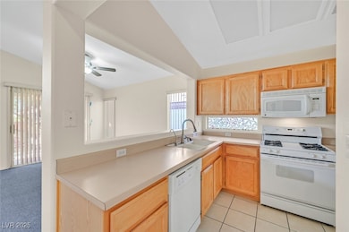 Kitchen with white appliances, light brown cabinetry, vaulted ceiling, light countertops, and a peninsula