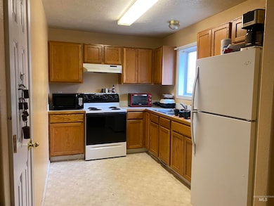 Kitchen with freestanding refrigerator, electric stove, brown cabinets, and a textured ceiling