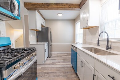 Kitchen featuring appliances with stainless steel finishes, white cabinets, light stone countertops, light wood-type flooring, and beamed ceiling