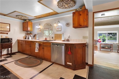 Kitchen with light countertops, brown cabinets, stainless steel dishwasher, crown molding, and black microwave