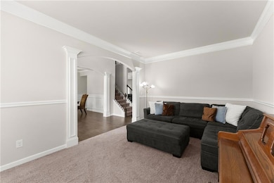 Living area with decorative columns, arched walkways, crown molding, carpet, and stairway