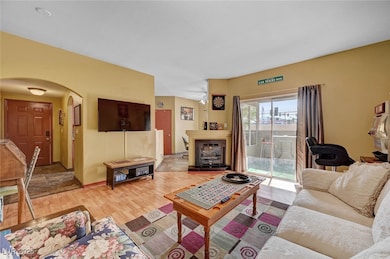 Living area with arched walkways, a fireplace with raised hearth, light wood-style floors, and baseboards