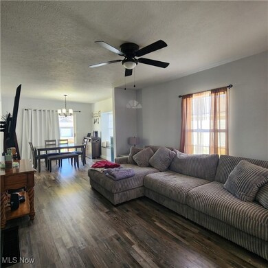 Living area with a textured ceiling, dark wood-style floors, a ceiling fan, and a chandelier