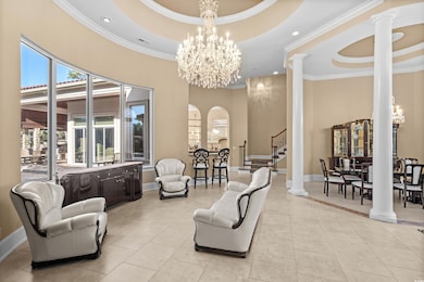 Living area with decorative columns, a tray ceiling, crown molding, a chandelier, and stairway