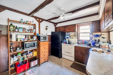 Kitchen with white range with electric cooktop, light countertops, beam ceiling, stainless steel microwave, and freestanding refrigerator