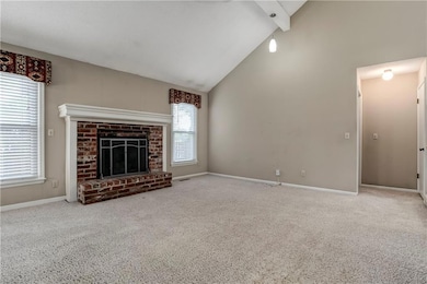Spacious family room featuring vaulted ceilings, neutral paint tones, and a brick fireplace framed by white trim and dual windows for balanced light.