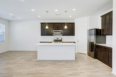 Kitchen with dark brown cabinetry, pendant lighting, appliances with stainless steel finishes, recessed lighting, and a kitchen island with sink