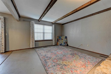 Unfurnished room featuring beamed ceiling, a textured wall, and baseboards