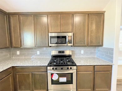 Kitchen with stainless steel appliances, light stone countertops, backsplash, and brown cabinetry