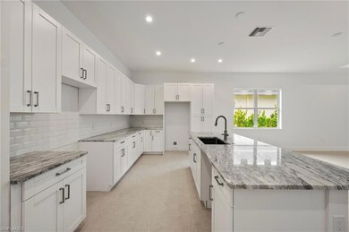 Kitchen featuring tasteful backsplash, white cabinets, light stone countertops, recessed lighting, and an island with sink