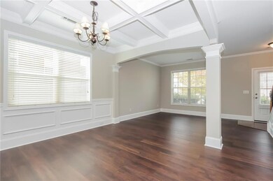 Unfurnished living room featuring ornate columns, arched walkways, coffered ceiling, healthy amount of natural light, and a chandelier