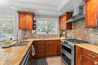 Kitchen featuring appliances with stainless steel finishes, ornamental molding, wall chimney range hood, decorative backsplash, and light stone countertops