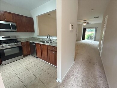 Kitchen featuring appliances with stainless steel finishes, light stone counters, ceiling fan, light carpet, and open floor plan