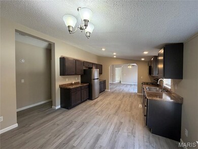 Kitchen with dark countertops, light wood finished floors, freestanding refrigerator, dark brown cabinets, and a textured ceiling