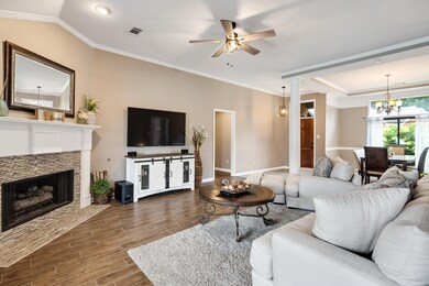 Living room with wood finished floors, a tiled fireplace, crown molding, a ceiling fan, and a chandelier