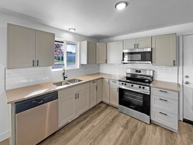 Kitchen featuring appliances with stainless steel finishes, light wood-style floors, backsplash, and light stone counters