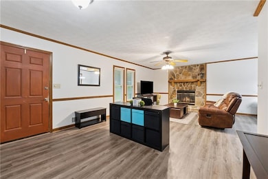 Living area with wood finished floors, ceiling fan, baseboards, crown molding, and a fireplace
