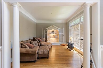 Living room with ornate columns, light wood finished floors, and crown molding