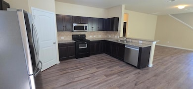 Kitchen featuring stainless steel appliances, decorative backsplash, dark wood finished floors, a peninsula, and light stone counters