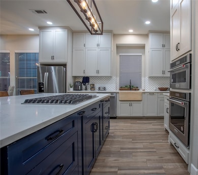 Kitchen with light stone countertops, stainless steel appliances, pendant lighting, tasteful backsplash, and light wood finished floors