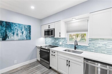Kitchen featuring a sink, backsplash, appliances with stainless steel finishes, white cabinets, and baseboards