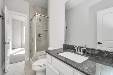 This is a modern guest bathroom featuring a glass-enclosed shower, a white vanity with dark granite countertop, and a large mirror. The space is finished with neutral tones and tile flooring.
