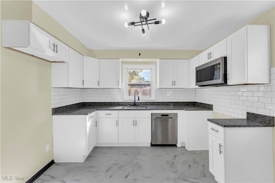 Kitchen with dark stone counters, appliances with stainless steel finishes, white cabinetry, and tasteful backsplash