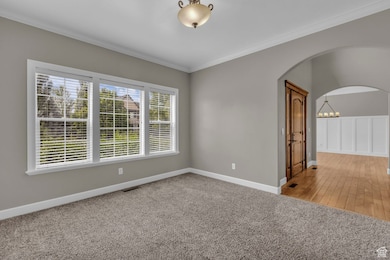 Spare room featuring light carpet, ornamental molding, arched walkways, and a chandelier