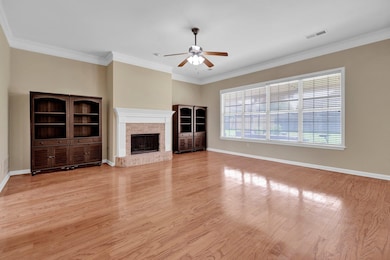 Unfurnished living room featuring a ceiling fan, wood finished floors, a fireplace, crown molding, and baseboards