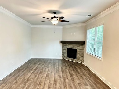 Unfurnished living room with ceiling fan, wood finished floors, crown molding, and a brick fireplace
