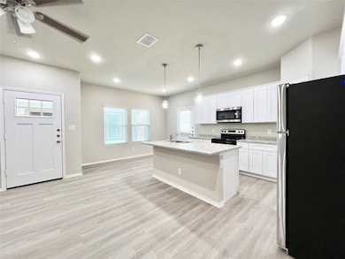 Kitchen featuring stainless steel appliances, a kitchen island with sink, light wood-style flooring, white cabinetry, and hanging light fixtures