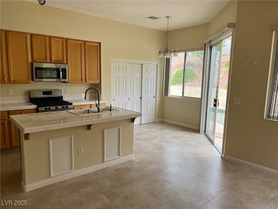 Kitchen with appliances with stainless steel finishes, brown cabinets, pendant lighting, a chandelier, and tile counters