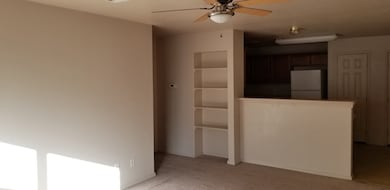 Unfurnished living room featuring light carpet, a ceiling fan, and built in shelves