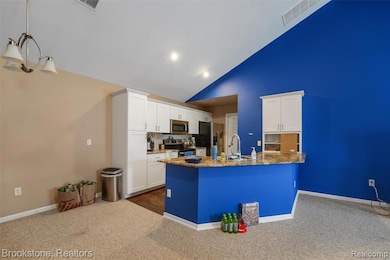 Kitchen featuring dark colored carpet, white cabinets, high vaulted ceiling, decorative backsplash, and a peninsula
