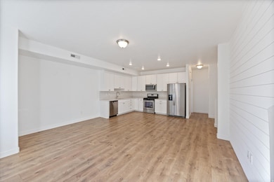Kitchen with white cabinets, appliances with stainless steel finishes, light countertops, light wood-style flooring, and tasteful backsplash