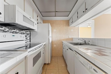 Kitchen featuring white appliances, a sink, tile c