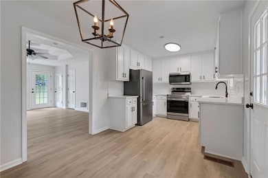 Kitchen with stainless steel appliances, a sink, light countertops, light wood-style flooring, and white cabinets