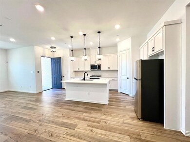Kitchen with a sink, stainless steel appliances, light countertops, white cabinets, and light wood-style floors