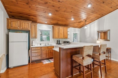 Kitchen with freestanding refrigerator, wood ceiling, stainless steel microwave, a breakfast bar, and light countertops