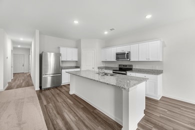 Kitchen with white cabinetry, appliances with stainless steel finishes, light stone countertops, dark wood-style floors, and recessed lighting
