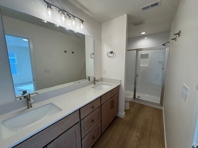 Bathroom with a textured ceiling, double vanity, a stall shower, and light wood-style floors