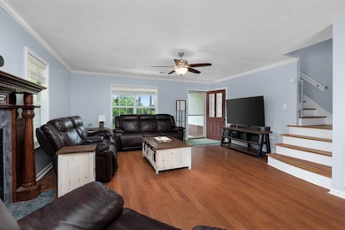Living room with wood finished floors, stairway, a ceiling fan, ornamental molding, and a textured ceiling