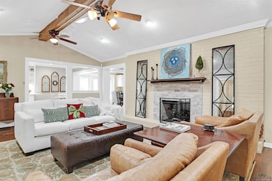 Living room featuring vaulted ceiling with beams, crown molding, a fireplace, and light wood-type flooring