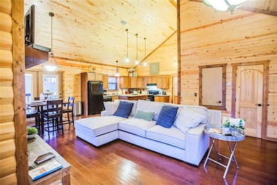 Living room with wooden walls, high vaulted ceiling, dark wood-style flooring, and wood ceiling